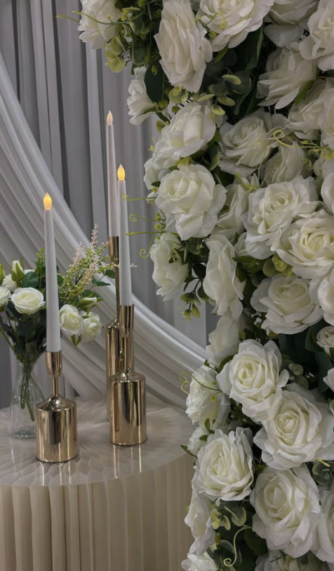 Gold candlesticks beside a wall of white roses and soft drapery