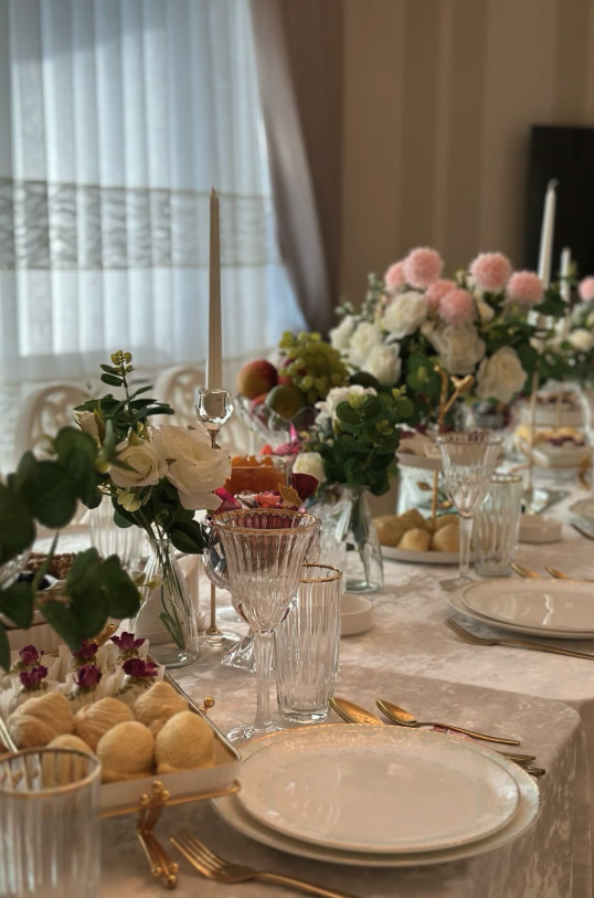 Long dining table dressed in white linen with gold cutlery, candles and pink and white florals