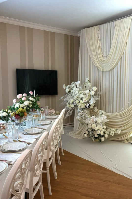 Wedding hall with a long white table, draped backdrop and floral arch